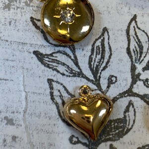 May include: Two gold-tone charms, one round with a clear rhinestone and the other a heart shape.
