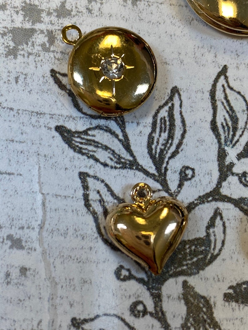 May include: Two gold-tone charms, one round with a clear rhinestone and the other a heart shape.