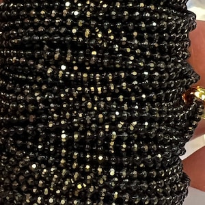 May include: A strand of black faceted beads with a gold shimmer. The beads are small and round, and they are strung together on a clear thread.