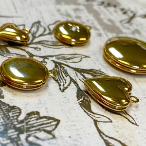 May include: Five gold-toned locket pendants in different shapes, including a heart, circle, and oval. The lockets are all closed and have a shiny finish.