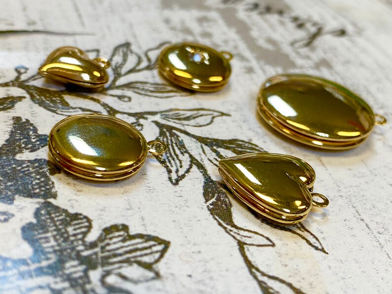 May include: Five gold-toned locket pendants in different shapes, including a heart, circle, and oval. The lockets are all closed and have a shiny finish.