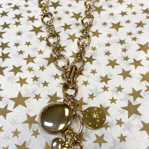 May include: A gold chain necklace with multiple charms, including a heart, a round charm with a small diamond, and a round charm with a snowflake design.
