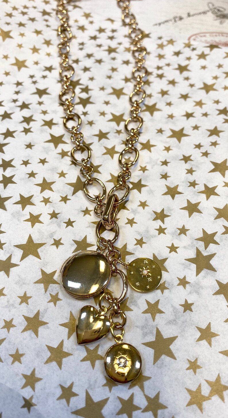 May include: A gold chain necklace with multiple charms, including a heart, a round charm with a small diamond, and a round charm with a snowflake design.