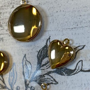 May include: Two gold-tone metal charms, one round and one heart-shaped. Both charms have a loop for attaching to a necklace or bracelet.