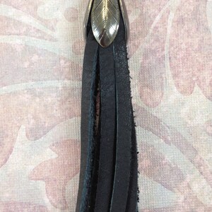 K&ouml;nnte beinhalten: Ein schwarzer Lederquaste mit einem silbernen, blattf&ouml;rmigen Oberteil. Die Quaste ist etwa 15 cm lang und hat einen ausgefransten Rand.