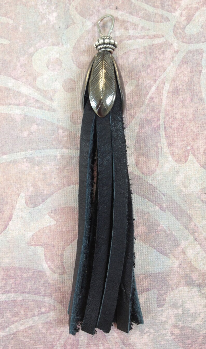 K&ouml;nnte beinhalten: Ein schwarzer Lederquaste mit einem silbernen, blattf&ouml;rmigen Oberteil. Die Quaste ist etwa 15 cm lang und hat einen ausgefransten Rand.