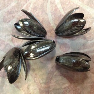 K&ouml;nnte beinhalten: Vier schwarze, metallene, blumenf&ouml;rmige Verzierungen mit strukturierter Oberfl&auml;che.
