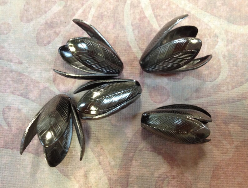 K&ouml;nnte beinhalten: Vier schwarze, metallene, blumenf&ouml;rmige Verzierungen mit strukturierter Oberfl&auml;che.