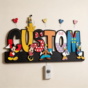 May include: A wooden wall sign featuring the word CUSTOM in large, colourful letters decorated with Disney character patterns. Mickey, Minnie, Pluto, Goofy, Daisy, and Donald Duck are depicted alongside small balloon icons. A white light switch is below.