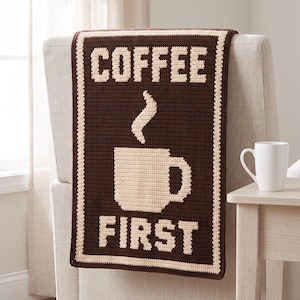 May include: A rectangular crochet wall hanging or throw featuring a dark brown background with a cream-colored border. The center displays a cream-colored graphic of a steaming coffee mug with the text COFFEE above and FIRST below in cream.