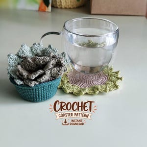 May include: A clear glass mug sits on a round, light green crocheted coaster with a scalloped edge. Beside it is a teal crocheted pot containing a multi-layered, sage green and grey crocheted succulent. Text reads: CROCHET COASTER PATTERN INSTANT DOWNLOAD.