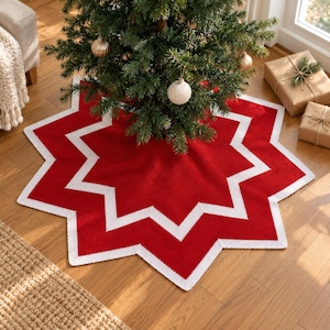 Peut inclure: Une jupe de sapin de Noël en forme d'étoile avec un centre rouge vif et une bordure blanche contrastante. Le tissu présente un aspect texturé semblable à du tricot avec des pointes géométriques nettes rayonnant depuis l'ouverture centrale.