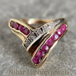May include: A gold V-shaped ring featuring two rows of round-cut red rubies and a central channel set with small clear diamonds. The metal band has a polished finish. The text Nihar Hiphop jewels is visible at the bottom of the image.