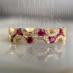 Op de afbeelding: Een gouden ring met een dubbel golvend ontwerp, geaccentueerd met ronde rode robijnen en kleine heldere steentjes. De tekst Nihar HipHop Jewels staat over de afbeelding heen. De ring heeft een gepolijste afwerking en een symmetrische structuur.
