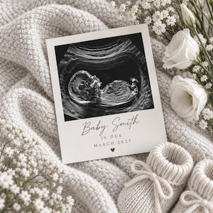 Może przedstawiać: Kwadratowa karta ogłoszeniowa z czarno-białym zdjęciem USG płodu. Tekst brzmi Baby Smith IS DUE MARCH 2027 z małą ikoną serca. Karta znajduje się obok pary kremowych dzianinowych bucików dziecięcych oraz białych kwiatów.