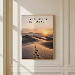 May include: A rectangular wall art print in a thin gold frame featuring a desert landscape at sunset with a line of footprints in the sand. The text reads: SMALL STEPS. BIG DISTANCE. CONSISTENCY TAKES YOU PLACES MOTIVATION NEVER WILL.