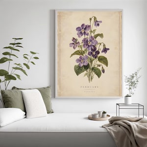 May include: A framed wall art print featuring a botanical illustration of purple violet flowers with green leaves on a beige background. The text FEBRUARY VIOLETS is printed in black below the floral arrangement, which is centered in the frame.