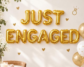 May include: Gold foil balloons spelling out the words JUST ENGAGED, accompanied by small heart-shaped wall decals and a line drawing of a diamond ring. The display includes white and gold balloons and a vase with white flowers.