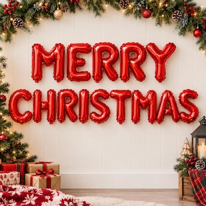 May include: Shiny red foil balloons spelling out MERRY CHRISTMAS are mounted on a white paneled wall. The display is framed by evergreen branches with red ornaments and pinecones, with wrapped gift boxes and a lantern below.
