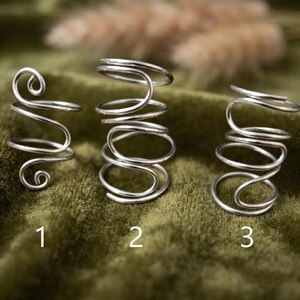 Puede incluir: Tres anillos de metal plateado etiquetados como uno, dos y tres. El anillo uno tiene un diseño en espiral con dos bucles. El anillo dos es una estructura alta en forma de resorte. El anillo tres consta de tres bucles de alambre apilados.