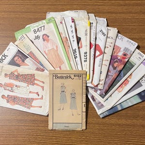 May include: A collection of vintage sewing patterns arranged in a fan shape. The envelopes feature various illustrations of dresses and garments, with brand names like Butterick, Simplicity, and Quick printed on the front along with pattern numbers.