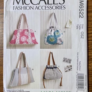 May include: McCall's M6522 Fashion Accessories sewing pattern envelope by Laura Ashley. The front displays four bag designs: a pink floral tote, a grey and white striped tote, a blue floral drawstring bag, and a navy and white striped drawstring bag.