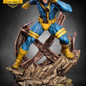 Può includere: Una statua da collezione dettagliata di un supereroe in costume blu e giallo con visiera rossa, in posa dinamica su una base rocciosa piena di detriti con un grande simbolo X. La figura ha i capelli castani e un'espressione urlante.
