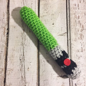 Puede incluir: Un juguete de sable de luz de crochet verde, gris y negro con un bot&oacute;n rojo.