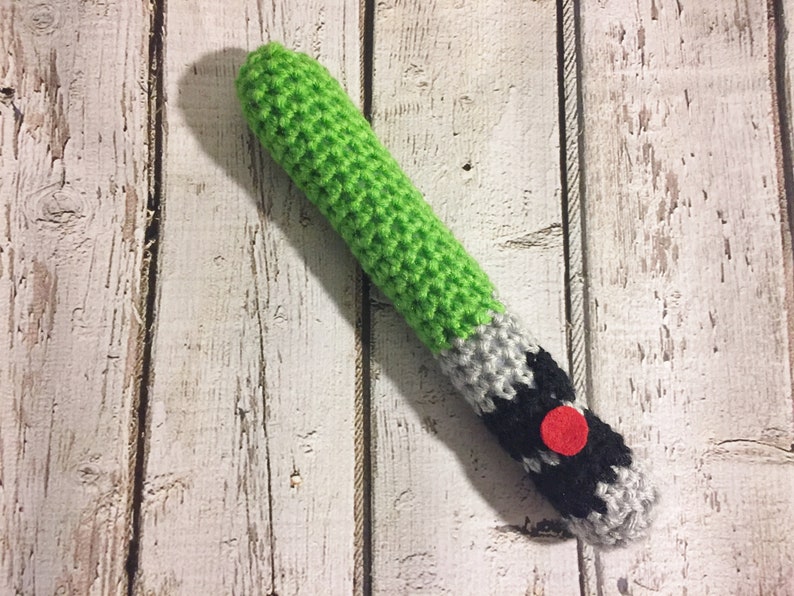 Puede incluir: Un juguete de sable de luz de crochet verde, gris y negro con un bot&oacute;n rojo.
