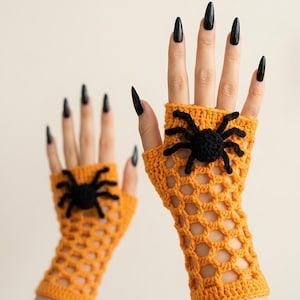 May include: A pair of orange fingerless gloves featuring a crocheted open-weave net pattern. Each glove is adorned with a three-dimensional black spider applique centered on the back of the hand, crafted from yarn with eight distinct legs.