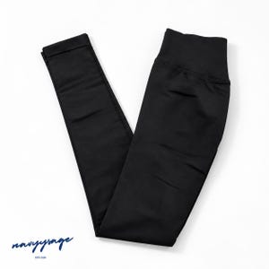 May include: Solid black leggings featuring a high-rise waistband and a slim-fit design. The fabric has a smooth, matte finish. In the bottom left corner, the text reads navysage ESTD 2026 in a dark blue script font with smaller block lettering.
