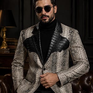 May include: A blazer featuring a beige and brown snakeskin pattern with contrasting black crocodile-textured lapels and chest panels. The garment is worn over a black turtleneck sweater and paired with dark sunglasses, showcasing a single-button closure.