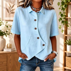 Puede incluir: Una camisa de manga corta en color azul claro con cuello clásico y una tapeta de botones asimétrica en la parte delantera con cinco botones de color marrón oscuro. La camisa tiene un dobladillo recto y se combina con vaqueros azul oscuro.
