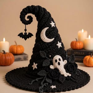 Op de afbeelding: Een zwarte gehaakte heksenhoed met een gebogen punt en een hangende zwarte vleermuisbedel. De hoed is versierd met witte gehaakte sterren, een halve maan en een spookfiguur, omringd door zwarte gehaakte rozen en bladeren aan takken.