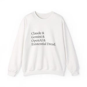 Könnte beinhalten: Ein weißes langärmeliges Sweatshirt mit Rundhalsausschnitt und schwarzem Textaufdruck auf der Vorderseite. Der Text lautet: Claude & Gemini & OpenAI & Existential Dread. Das Kleidungsstück hat gerippte Bündchen an Kragen, Ärmeln und Saum.