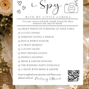 May include: A white wedding I Spy game card featuring black text and line art of a camera and hearts. The card lists photo prompts like group photo, couple, speech, dancer, sweet moment, selfie, guests, laughing, dancing, entrance, and a QR code.