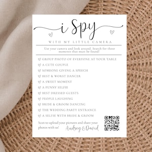 May include: A white rectangular wedding I Spy game card with black text and a QR code. The card lists photo prompts like group photo, cute couple, and bride and groom dancing. It includes the names Audrey and David and instructions to scan to upload photos.