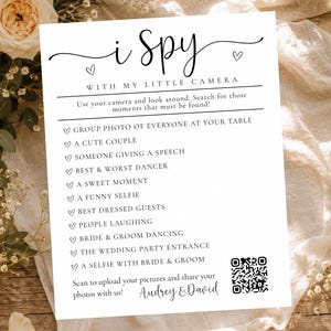 May include: A white rectangular wedding I Spy game card with black text and a QR code. The card lists photo prompts like group photo, couple, speech, dancer, sweet moment, selfie, guests, laughing, dancing, entrance, and selfie with bride and groom.