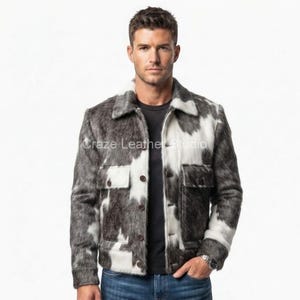 May include: A jacket featuring a cow-print pattern in shades of black, gray, and white. The garment has a collared neckline, a front button closure, and two chest pockets with buttoned flaps. The text Craze Leather Studio is visible on the front.