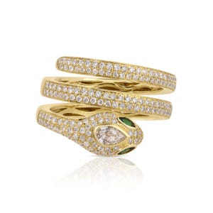 May include: A gold snake ring featuring a coiled design with pavé-set clear stones covering the entire band. The head of the snake is accented with a pear-shaped clear stone in the centre and two small green stones representing the eyes.