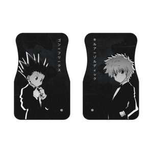May include: A pair of black car floor mats featuring white graphic illustrations of two anime characters in formal suits. The left mat displays a character with spiky hair and the text ゴン＝フリークス, while the right mat shows a character with short hair and the text キルア＝ゾルディック.
