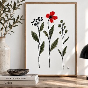 May include: A framed wall art print featuring a sketch-style illustration of three wildflowers on a white background. The central flower has bright red petals, while the surrounding stems and leaves are rendered in dark green and black ink lines.