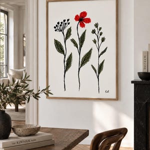 May include: A framed wall art print featuring a minimalist sketch of three botanical stems on a white background. The central stem displays a vibrant red flower, while the others are rendered in black ink with green leaves. The signature Kall is visible.