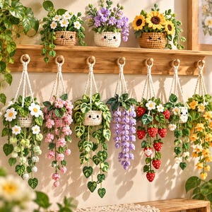 Könnte beinhalten: Eine Sammlung von zehn gehäkelten Topfpflanzen mit lächelnden Gesichtern, darunter Blumen, Erdbeeren und Ranken. Drei stehen auf einem Holzregal, während sieben an einem Wandregal aus Holz mit weißen Makramee-Schnüren hängend befestigt sind.
