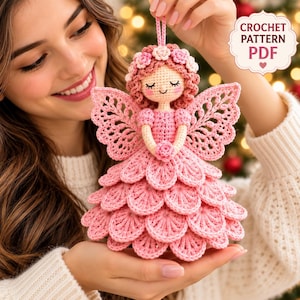 May include: A crocheted angel ornament featuring a pink layered petal skirt, intricate lace-like wings, and a head adorned with small pink flowers. The doll has closed eyes and rosy cheeks. Text in the upper right corner reads CROCHET PATTERN PDF.