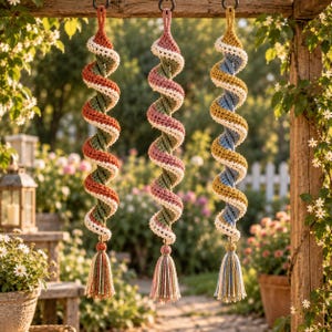 May include: Three hanging spiral decorations made of crocheted yarn. Each piece features a twisted design with a white border and a long tassel at the bottom. The colors include rust orange and green, dusty pink and green, and mustard yellow and blue.