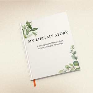 May include: A white hardback memory book titled MY LIFE, MY STORY: A Grandparent's Memory Book to Share, Laugh & Remember. The cover features watercolour green eucalyptus leaves in the top left and bottom right corners and an orange ribbon bookmark.