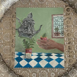 Puede incluir: Una pintura sobre una bandeja dorada texturizada muestra una tetera plateada flotando sobre una mesa con un mantel de cuadros azules y blancos. Una pequeña planta en una taza roja y blanca descansa sobre la mesa, mientras una mano sostiene otra.
