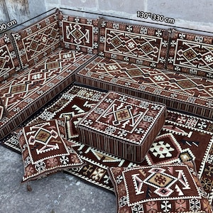 May include: An L-shaped floor sofa set featuring brown fabric with white, black, and tan geometric patterns. The set includes backrests, seat cushions, a square ottoman, and two rectangular pillows. Dimensions are 75 inches by 130 inches.