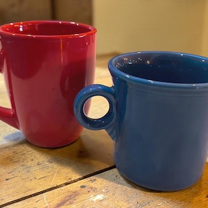 以下が含まれることがあります： 光沢のある赤いセラミック製のマグカップと、マットな質感の青いセラミック製のマグカップ。赤いマグカップには曲線的なハンドルがあり、青いマグカップには小さめの円形のハンドルが付いています。どちらも滑らかな仕上げで、飲み物を入れるためのシンプルな形状をしています。